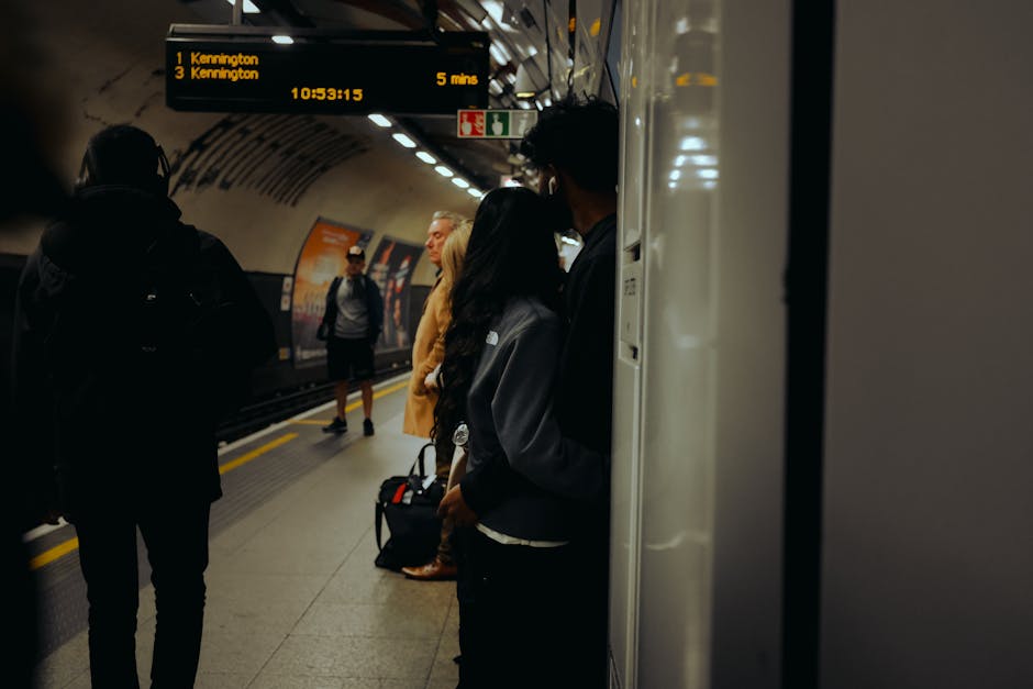 Inside a modern underground metro station, focusing on a clean, well-maintained platform with polished tiled flooring and stainless steel fixtures. Several passengers, some with backpacks and others w