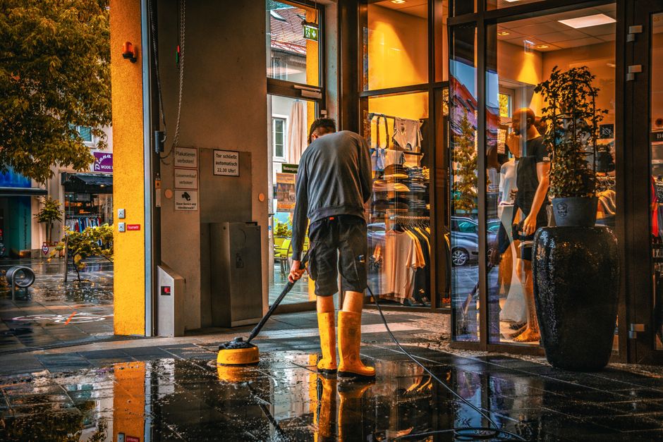 A professional cleaner from Deep Cleaning Kennington is engaged in surface cleaning using a vacuum cleaner with a handheld attachment. The individual is dressed in protective clothing, including glove